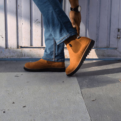Person wearing brown boots and blue jeans stepping onto a sidewalk.