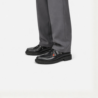 Black leather shoes worn with gray pants on a white background
