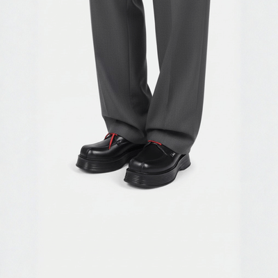 Black shoes with red laces worn with gray pants on a white background