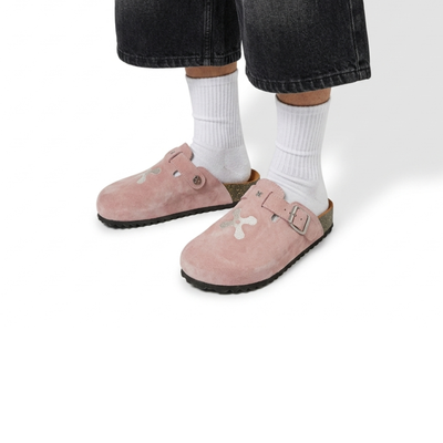 Pink suede clogs worn with white socks and black pants on a white background