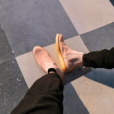 Person wearing brown shoes with yellow soles on a checkered pavement.