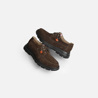 A pair of dark brown suede lace-up shoes with black rubber soles and small orange flower-shaped accents on the sides, displayed on a light gray background.