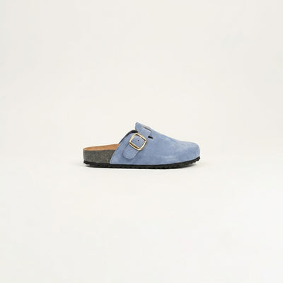 Blue suede clog shoe with a gold buckle on a light gray background