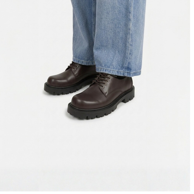 Brown leather shoes worn with blue jeans on a white background
