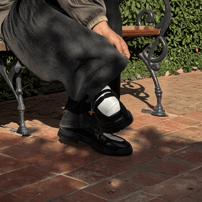 Person sitting on a bench wearing black shoes and white socks with a visible brand logo.