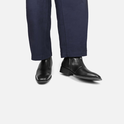 Black dress shoes worn with navy pants on a white background