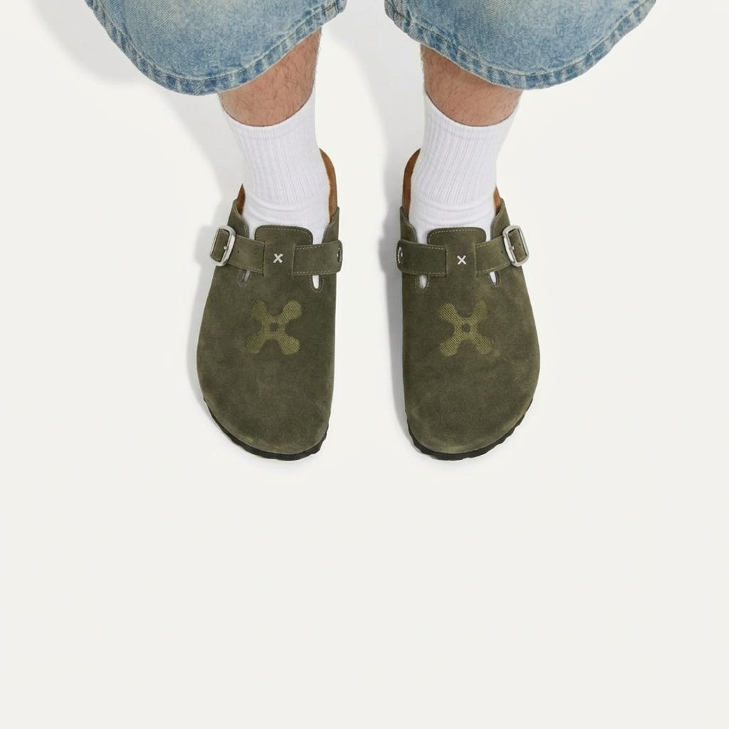 Green suede clogs worn with white socks and blue jeans on a white background