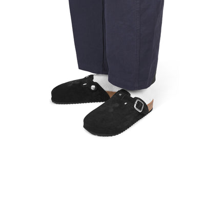 Black suede shoes with a buckle worn with navy pants on a white background
