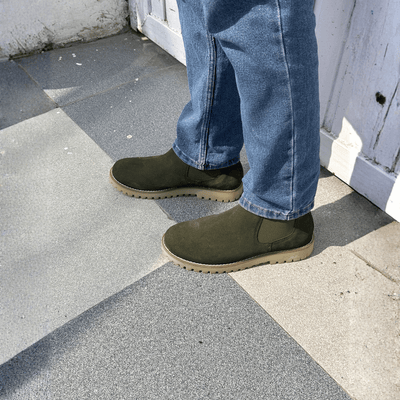 Person wearing green boots and blue jeans on a concrete surface.