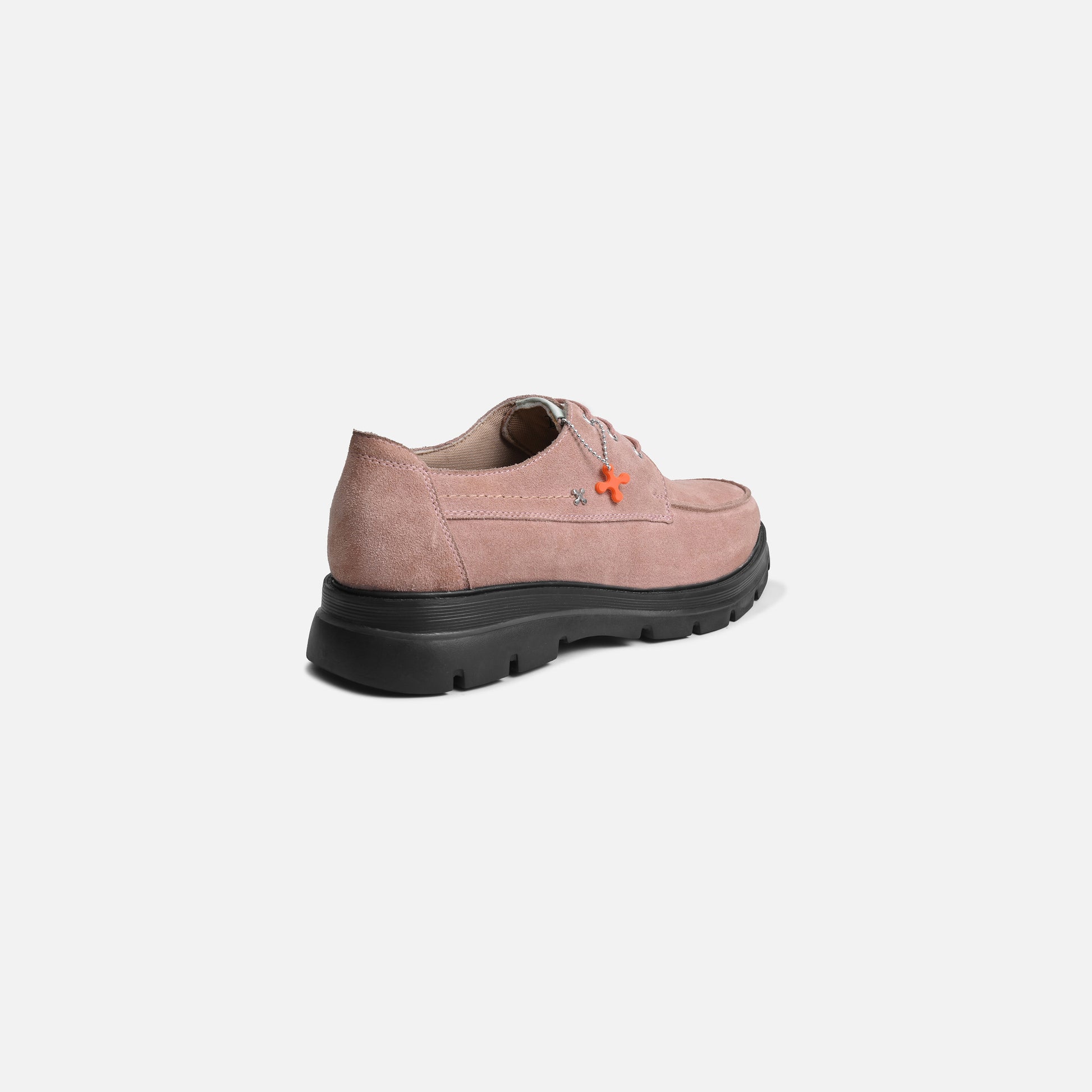 A single women's casual shoe shown from a rear three-quarter angle on a light gray background. The upper is a dusty pink suede-like material with a small orange embroidered logo, and it has a thick black lug sole.
