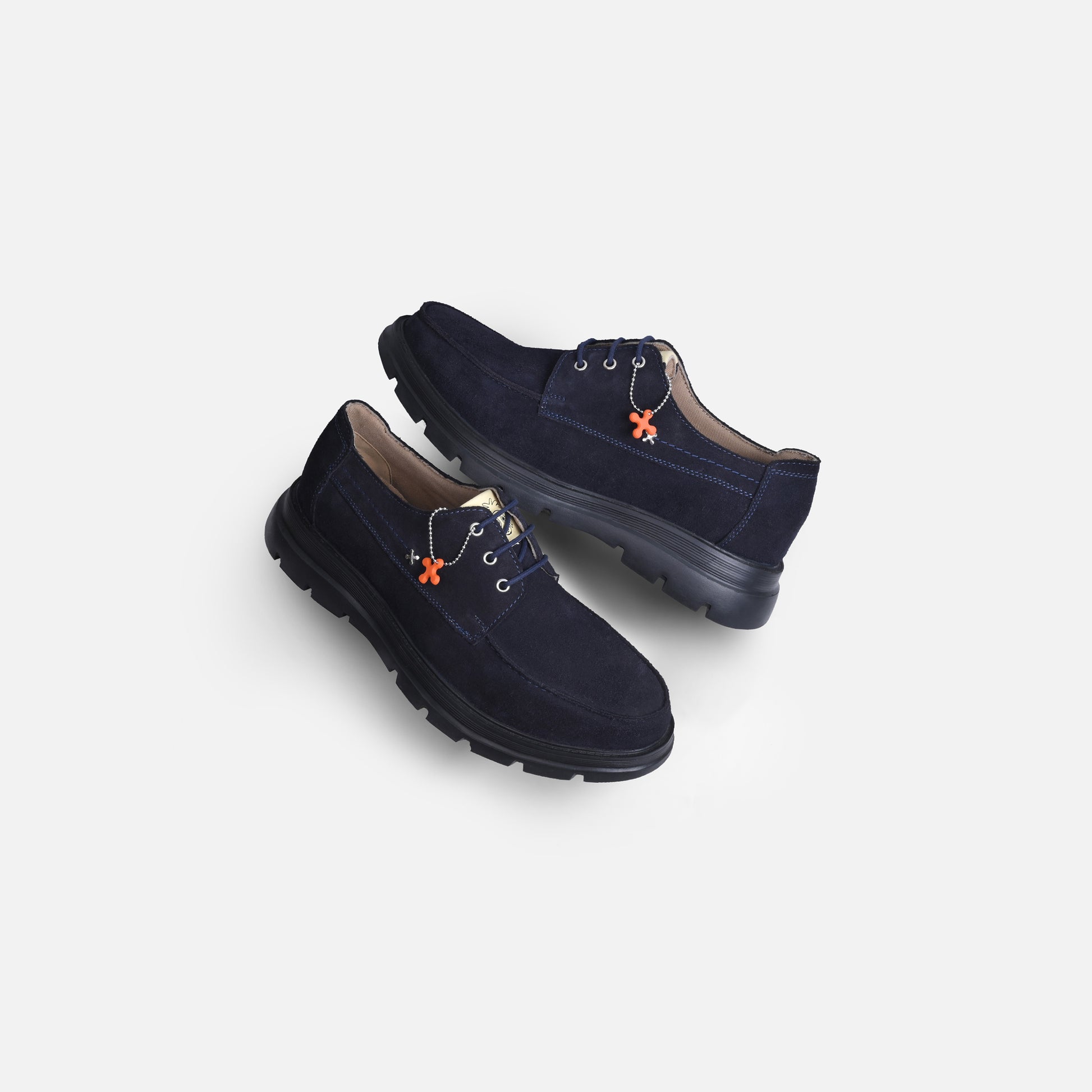 A pair of dark navy blue suede lace-up shoes with black soles and small orange decorative accents, displayed on a light gray background.