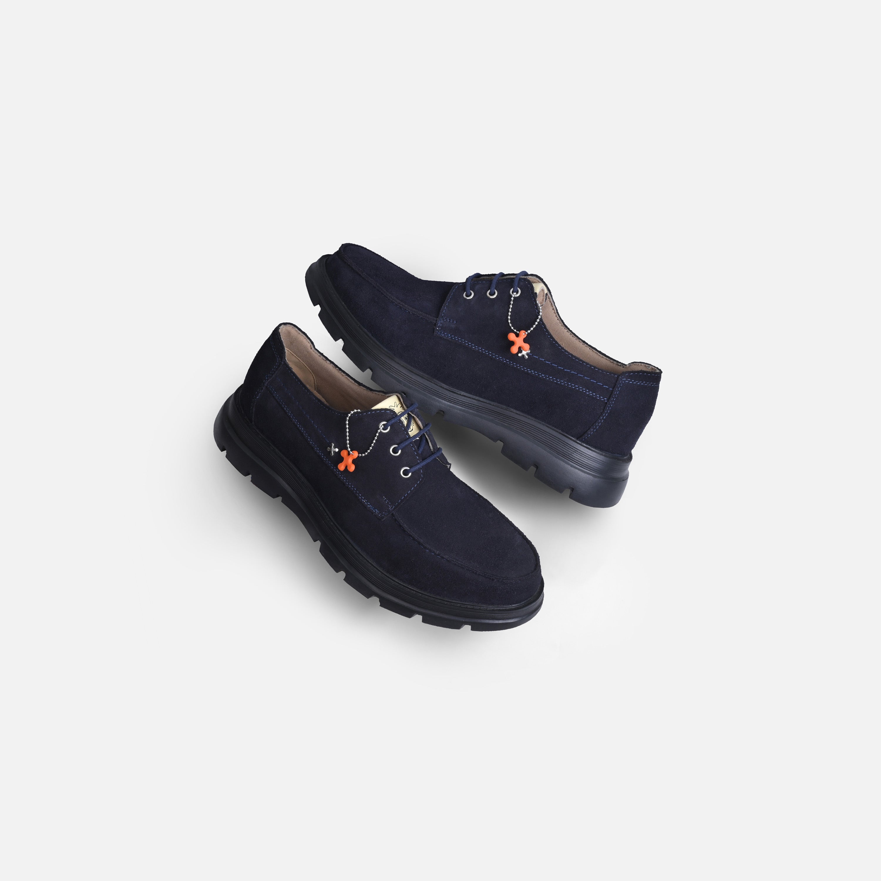 A pair of dark navy blue suede lace-up shoes with black soles and small orange decorative accents, displayed on a light gray background.