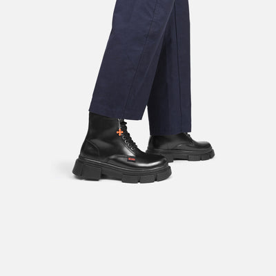 Black boots with a brand logo worn with navy pants on a light gray background