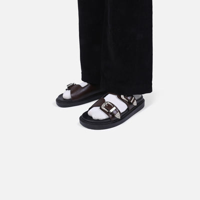 Black sandals with white soles worn with black pants on a light gray background