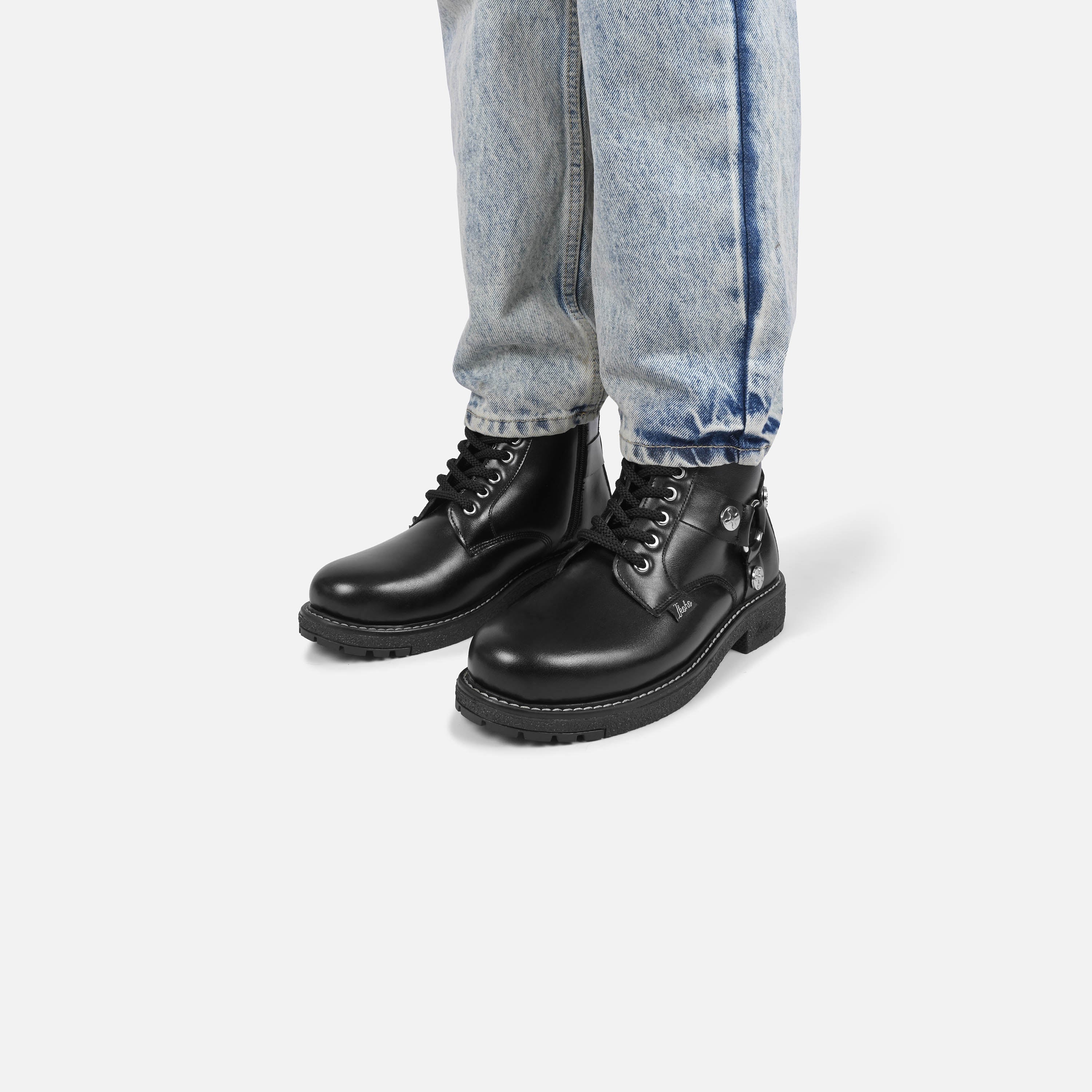 Black leather boots worn with light blue jeans on a white background