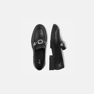 Black loafers with decorative buckle on a light gray background